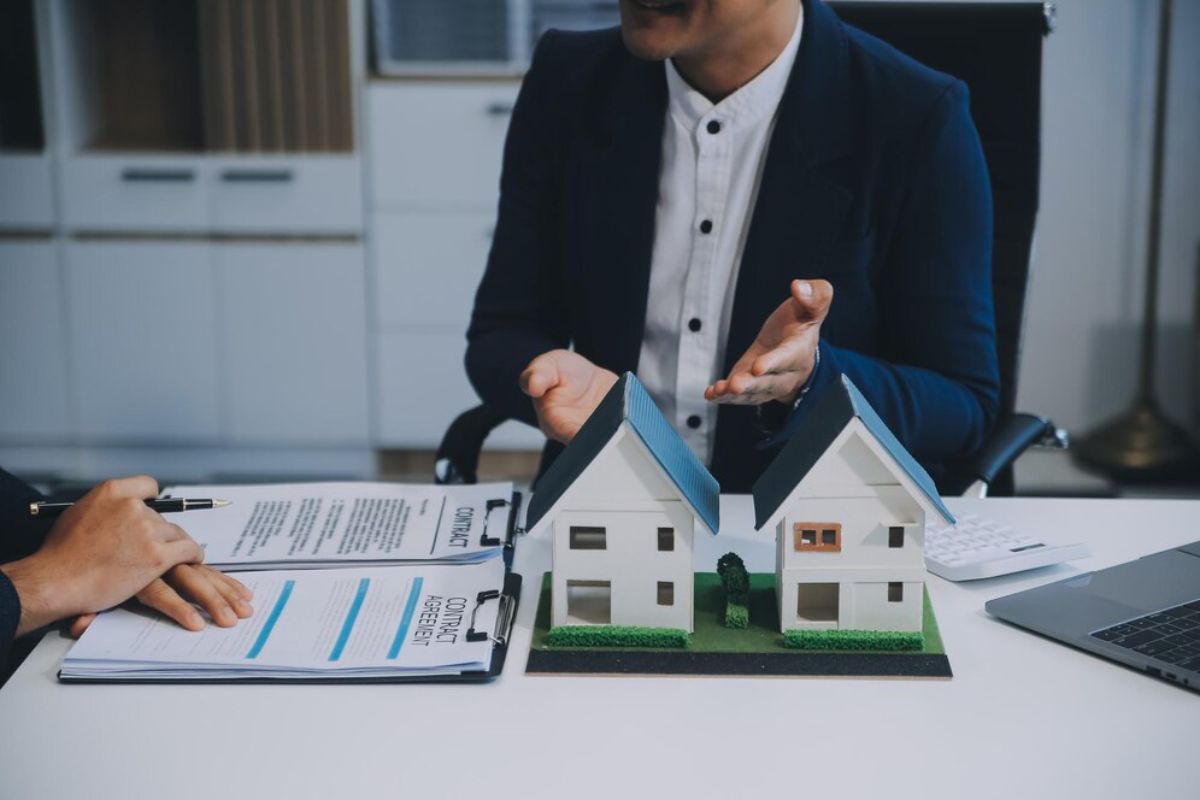 Man discussing paperwork with two model houses on table during a meeting in an office.