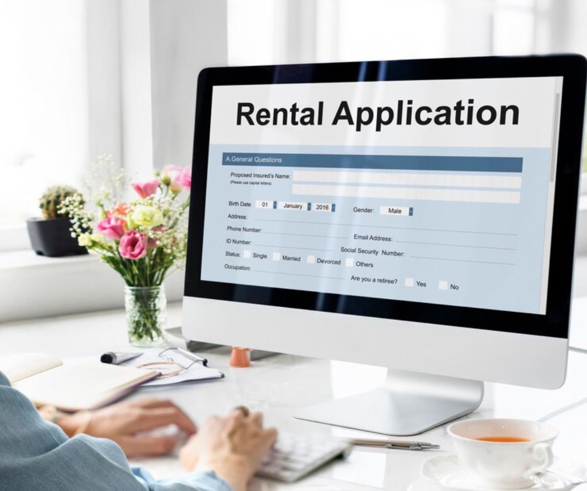 Person filling out a rental application form on a computer screen with tea and flowers nearby.