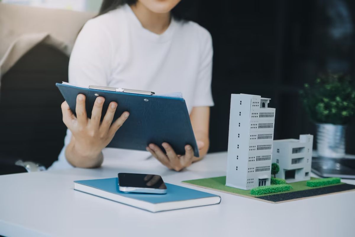 Person reviewing documents next to architectural models of buildings on a desk.