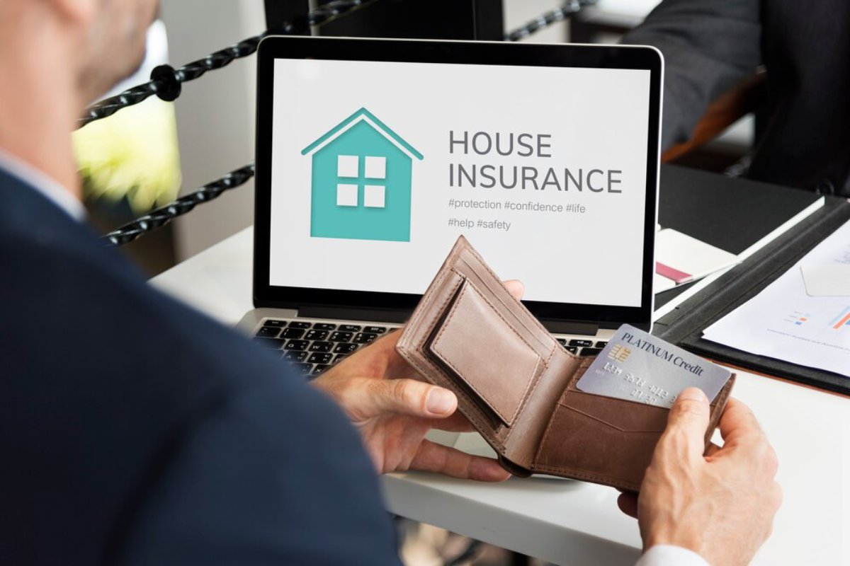 A businessman views a house insurance presentation on his laptop while holding a wallet and credit card.